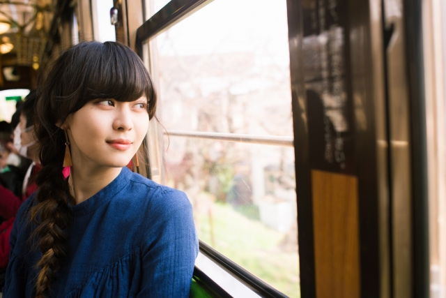 電車の窓の外の景色を眺める女性