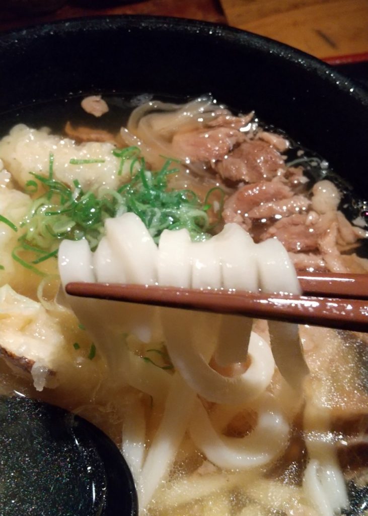 牛すじうどんの麺を箸で持ち上げる